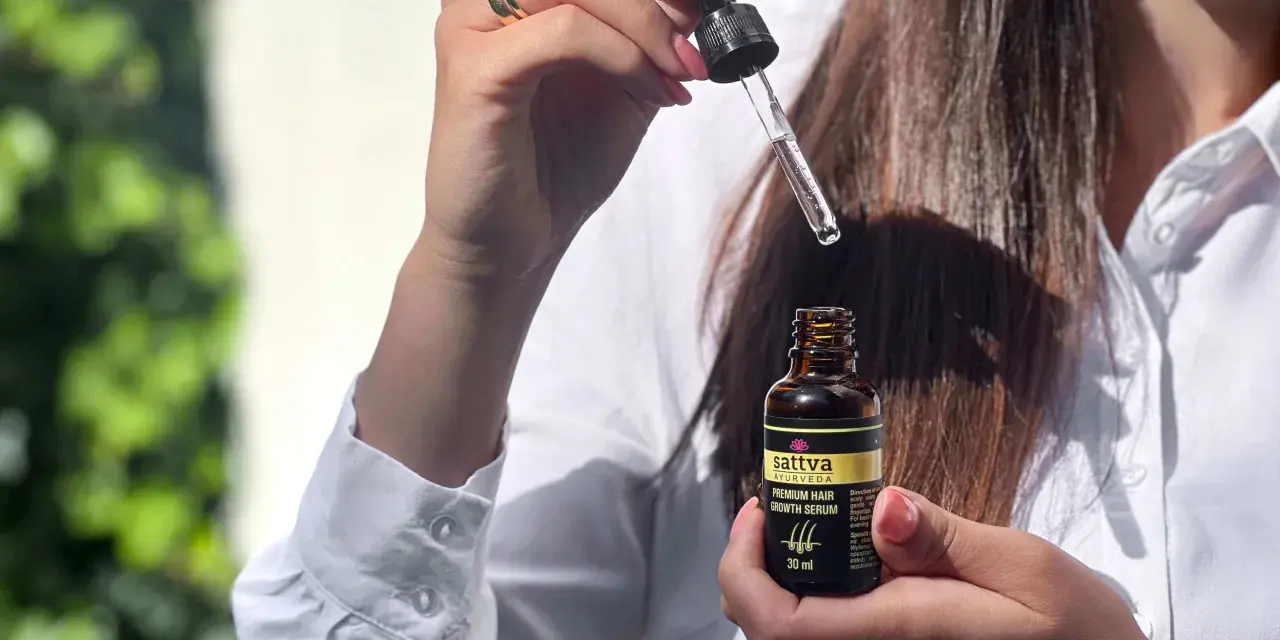Kobieta trzyma buteleczkę z olejkiem Sattva i pipetkę z serum do włosów.