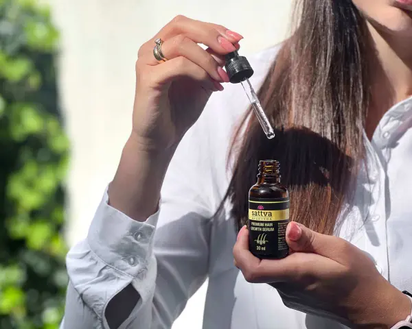 Kobieta trzyma buteleczkę z olejkiem Sattva i pipetkę z serum do włosów.